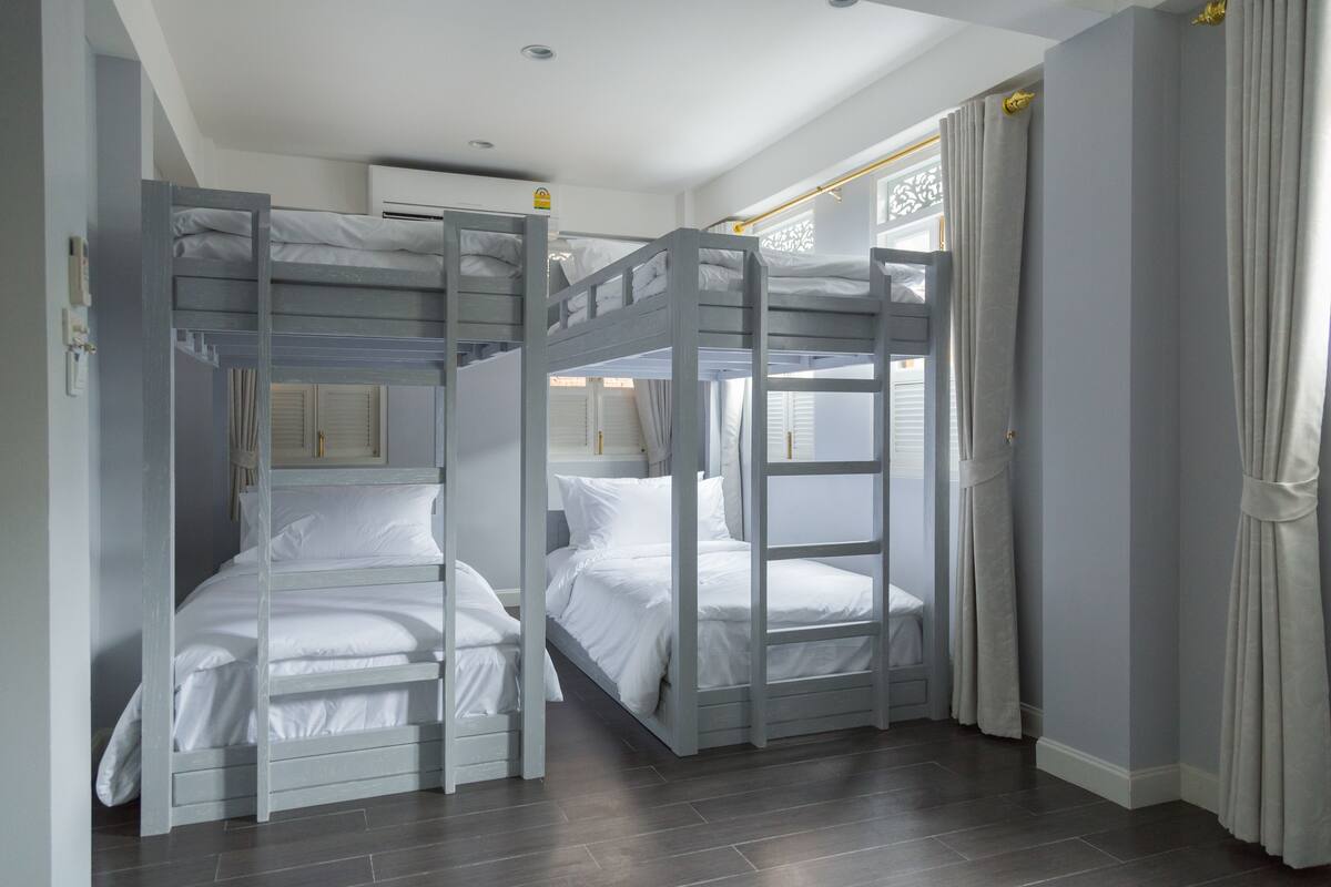 Une chambre avec deux lits superposés, une fenêtre avec des rideaux et un appareil de climatisation blanc.