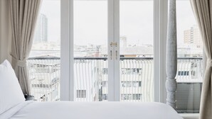 Une chambre d’hôtel avec un grand lit, un balcon donnant sur la ville et une fenêtre avec des rideaux.