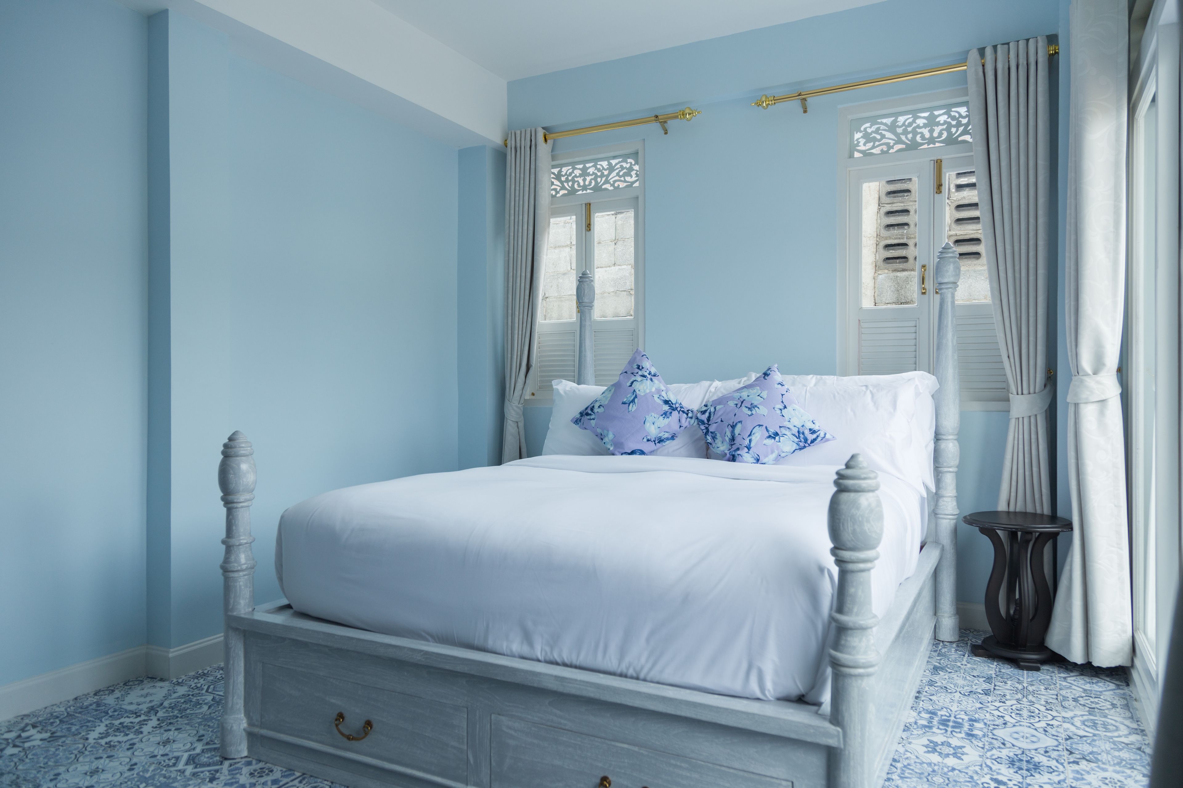 Un dormitorio con una cama blanca, paredes azules y baldosas de suelo con estampado.