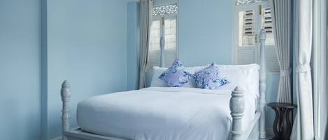 Un dormitorio con una cama blanca, paredes azules y baldosas de suelo con estampado.