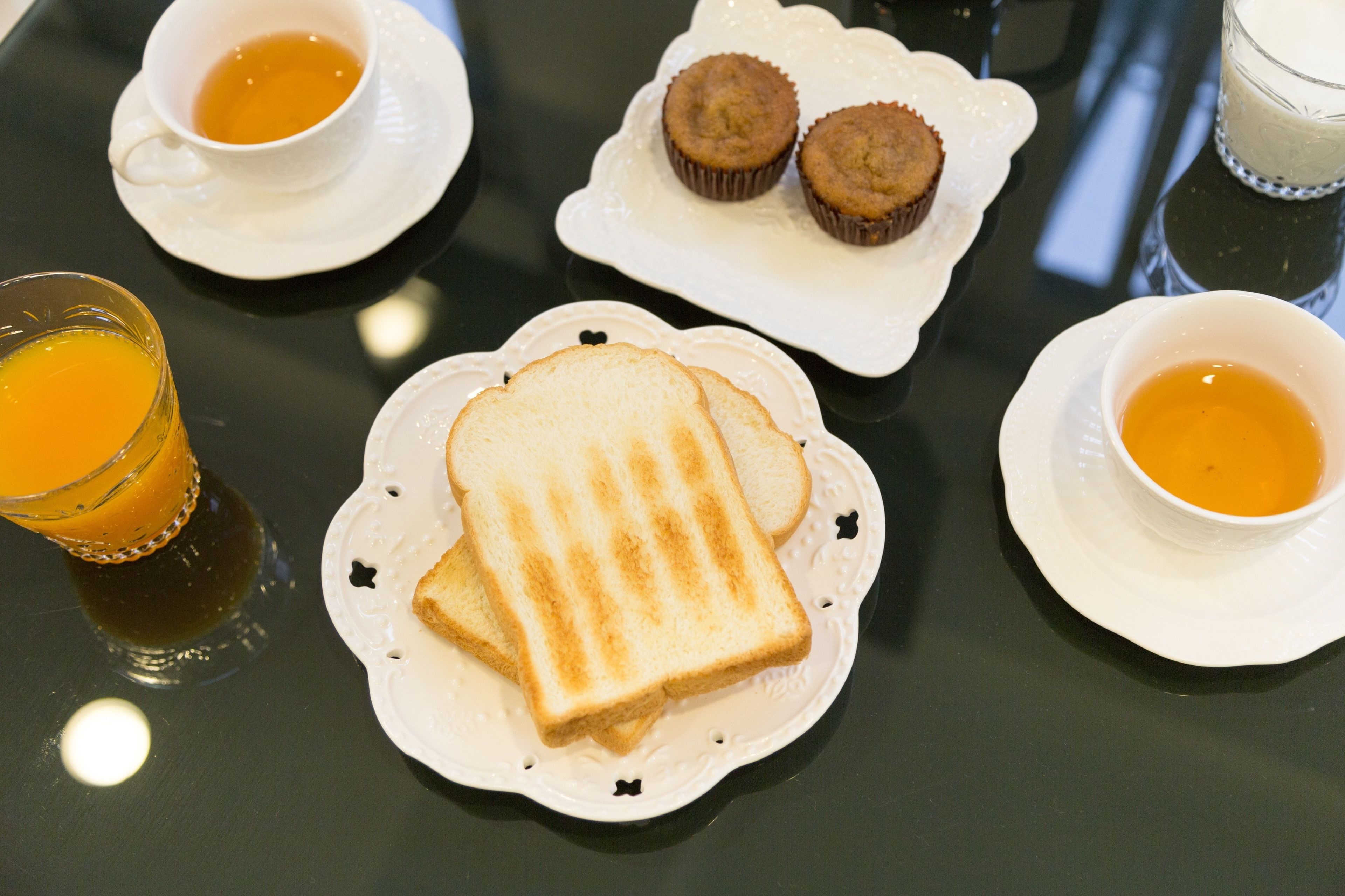 A table with a plate of toast, two muffins, and two cups of tea.