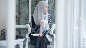 Une personne est assise à une table devant une tasse et une soucoupe, une cafetière et un verre.