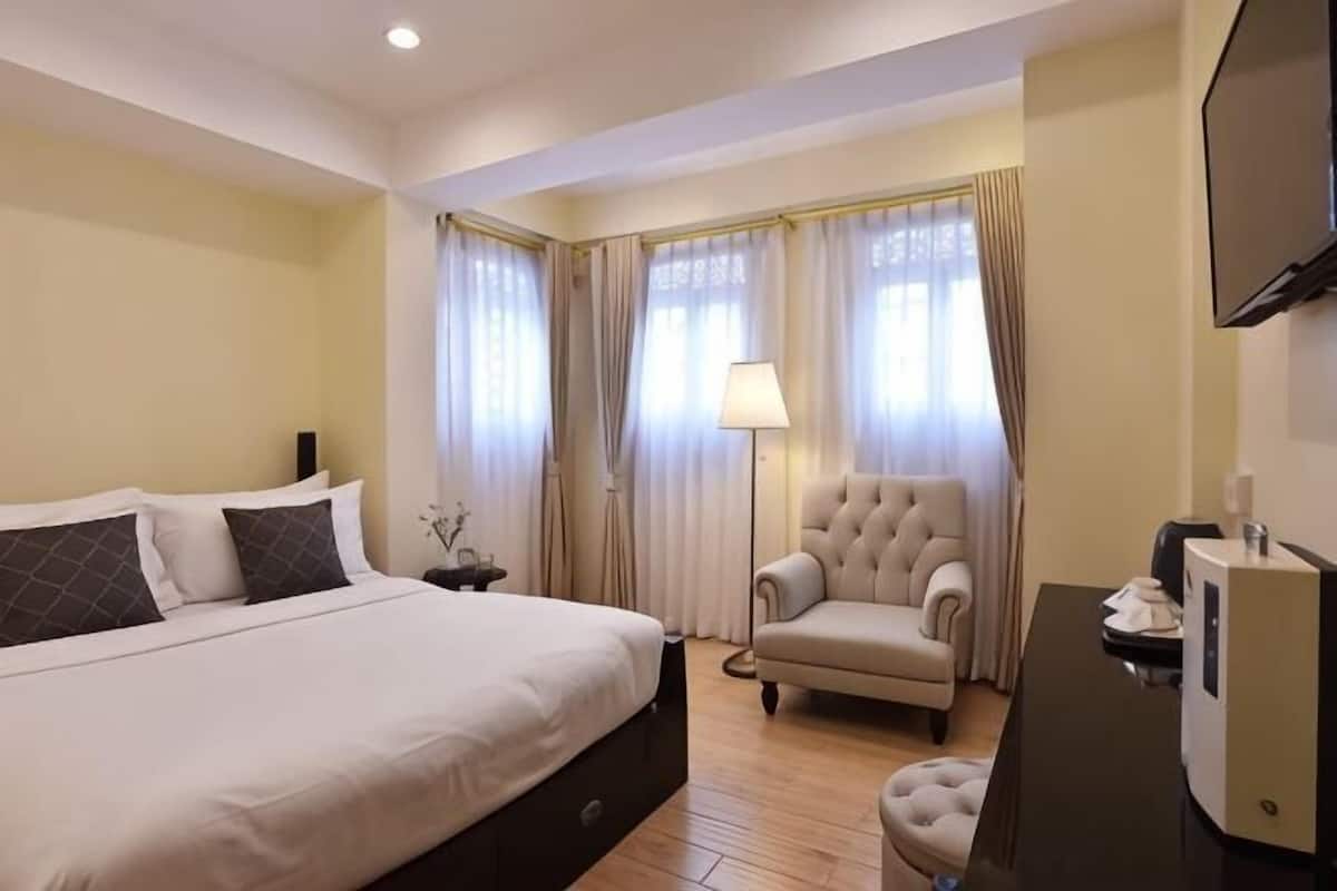 Une chambre d’hôtel avec un grand lit, un bureau avec un ordinateur, une chaise et des rideaux.