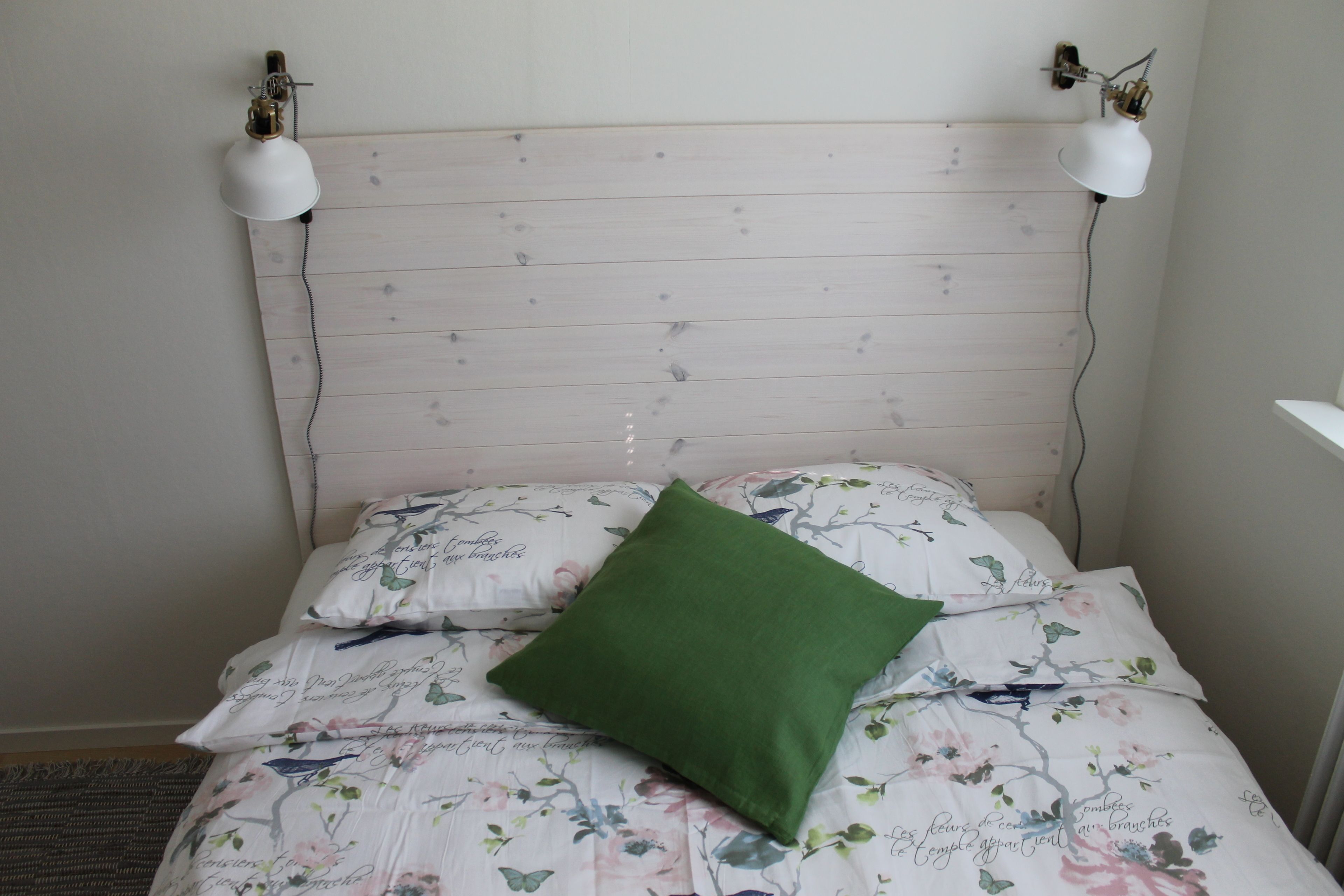 A bed with floral bedding and a green pillow, two wall-mounted lamps, and a wooden headboard.