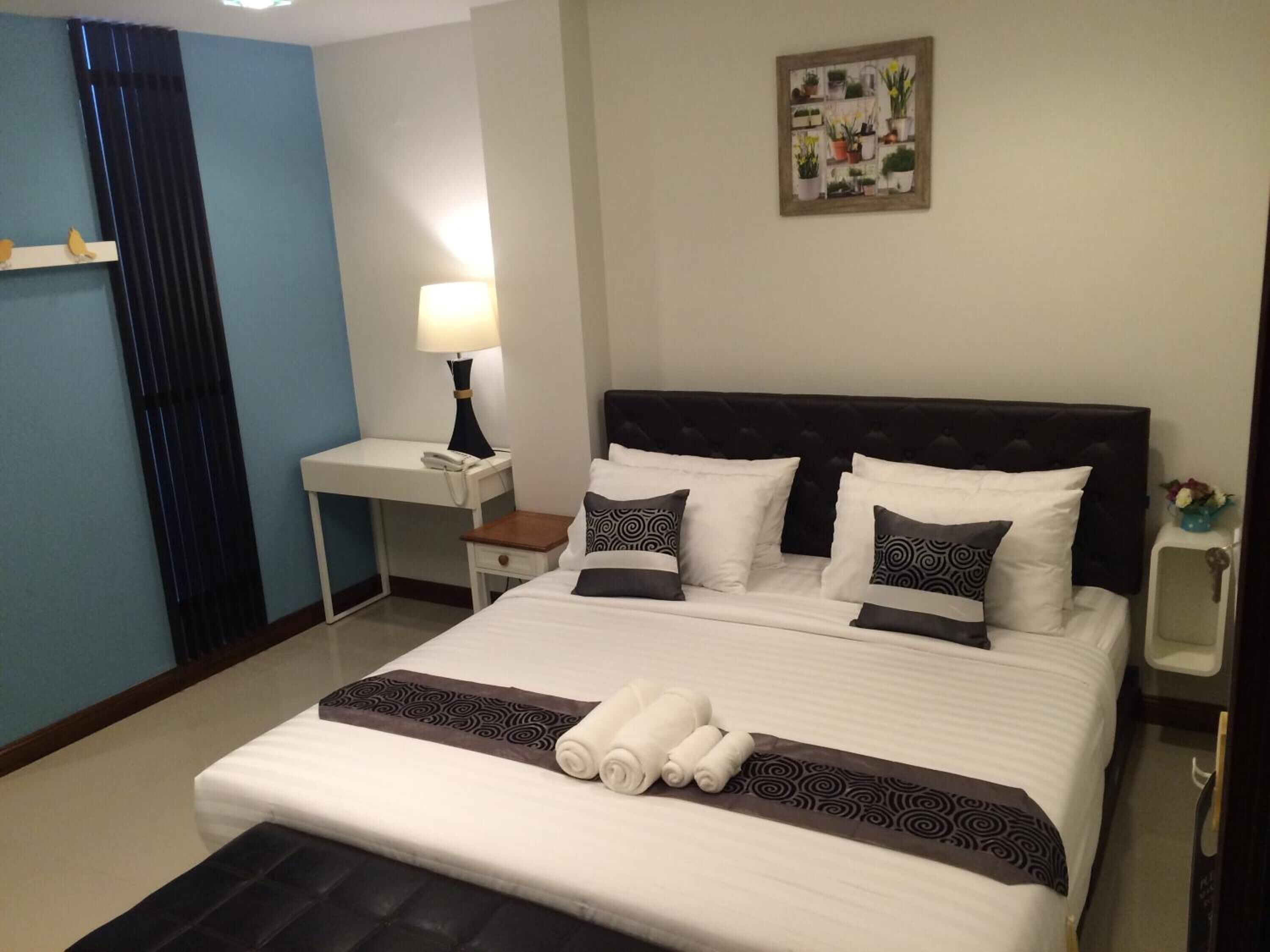 A neatly made bed with white and patterned pillows, a bedside table with a lamp, and a wall-mounted plant shelf.