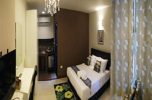 Quarto de hotel com cama, escrivaninha, cadeira, televisão e lustre.
