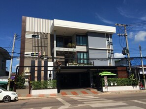 A modern two-story building with a covered entrance, a visible staircase, and a small garden area with plants. - Dino Studio (Kalasin)