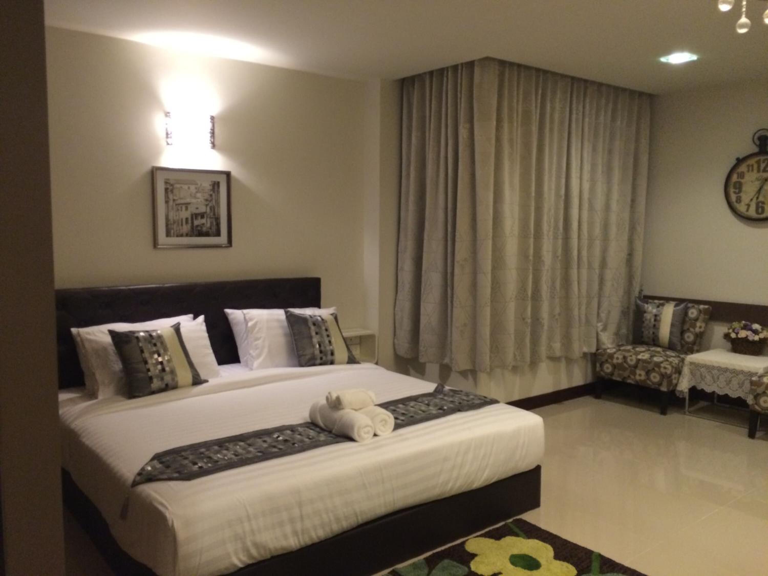 A hotel room with a bed, a clock, a picture on the wall, and a window with curtains.