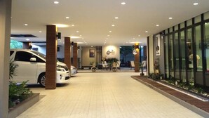 A hotel entrance with a paved driveway, a reception desk, and a glass facade. - Dino Studio (Kalasin)