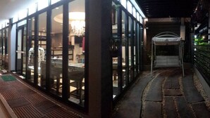 A corridor with glass storefronts, a covered seating area, and a patterned walkway. - Dino Studio (Kalasin)