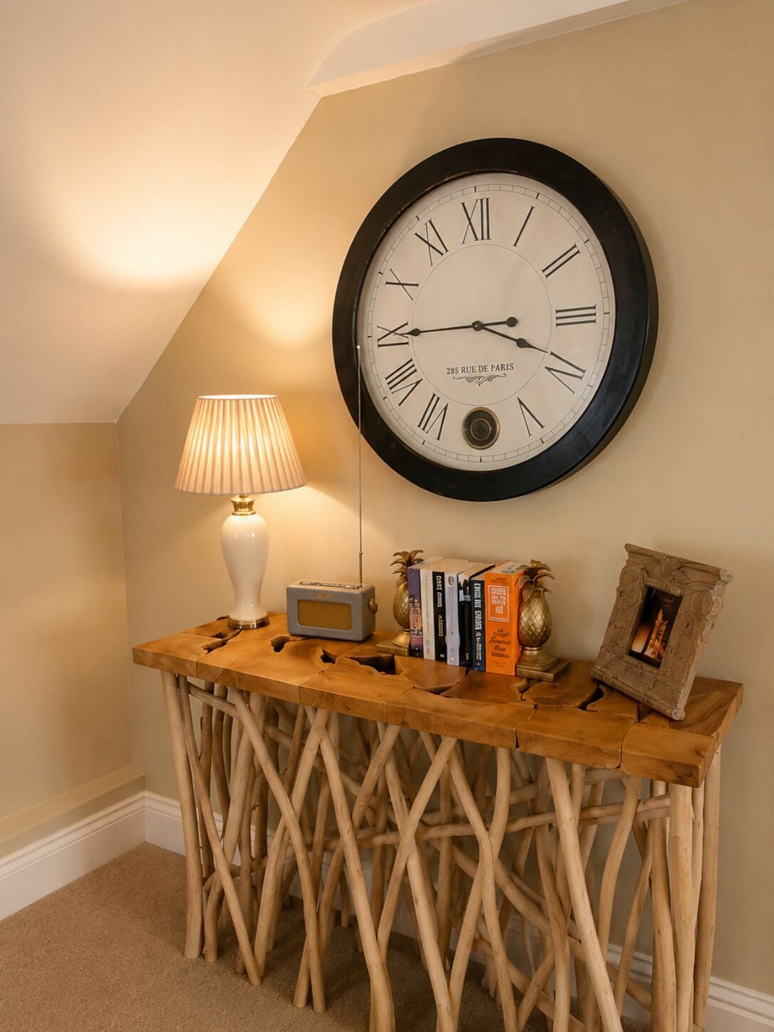 A wall-mounted clock, a lamp, books, and decorative items on a wooden console table.