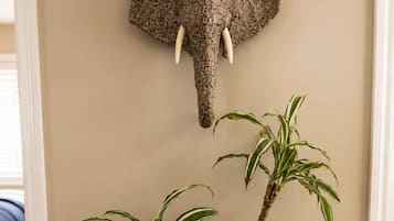 A potted plant with variegated leaves on a wooden stand, a textured elephant head decoration on the wall, and a beige wall.