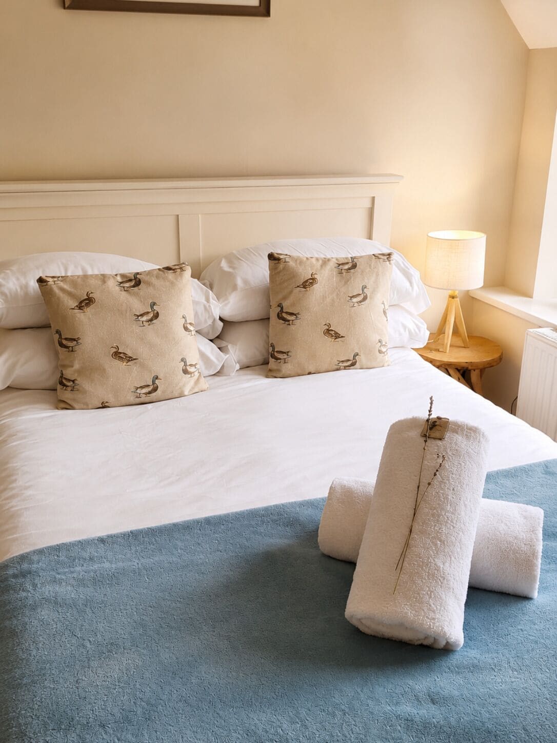 Quarto de hotel com cama, almofadas, luminária e toalhas.