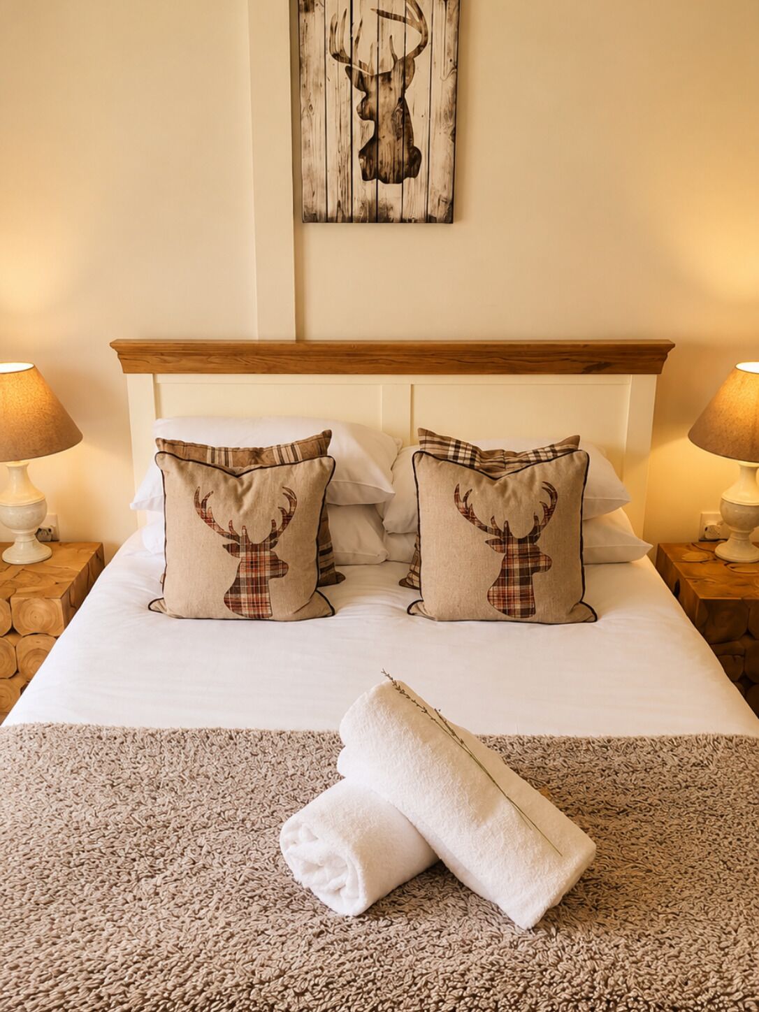 A neatly made bed with two pillows featuring a deer design, a wooden headboard, and a wall-mounted deer artwork.