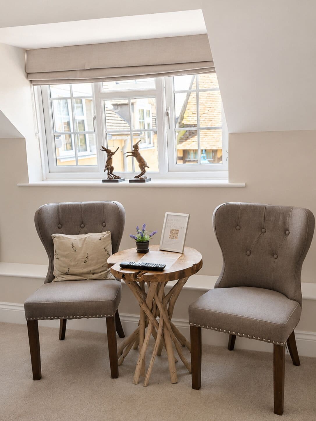 A room with two upholstered chairs, a small round table, and a window with a view of buildings.