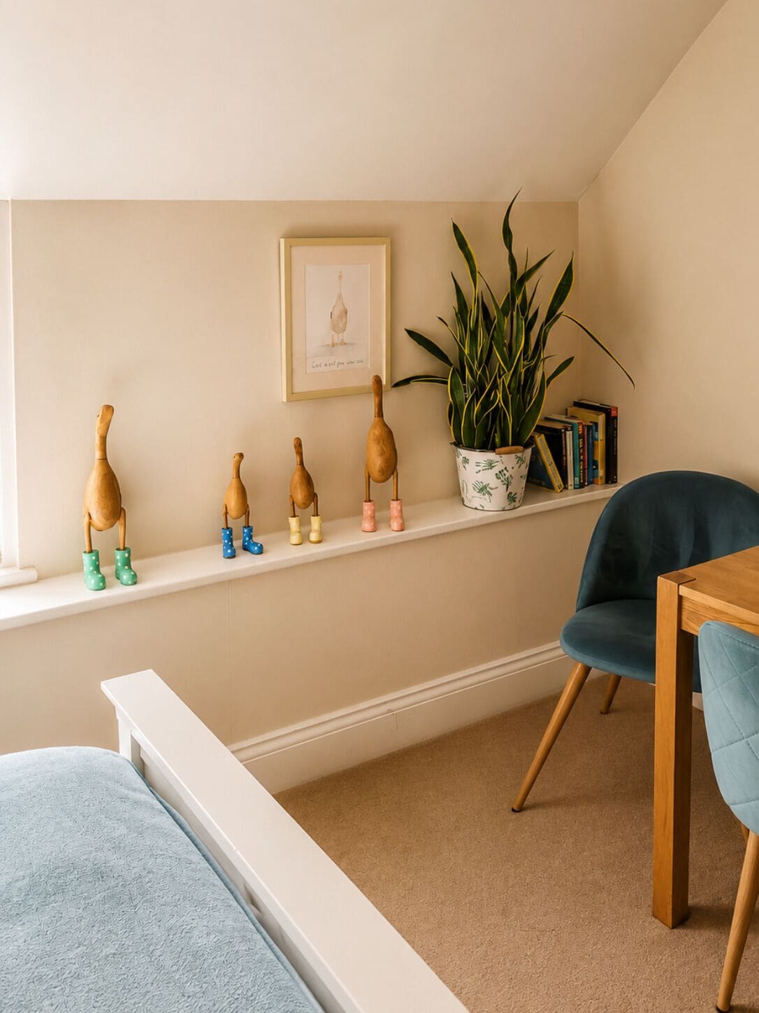 A room with a white bench, a blue chair, a wooden table, a potted plant, and a shelf with wooden figures and books.