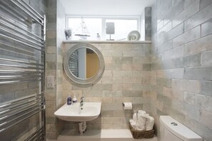 A bathroom with a white sink, a round mirror, a toilet, and a window above the sink. - The Lodge at Broadway (Broadway)
