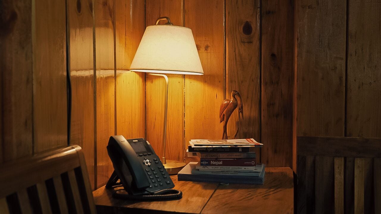 A wooden room with a lamp, a telephone, and a stack of books.