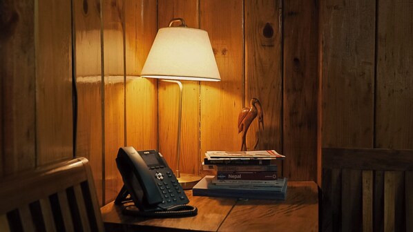 A wooden room with a lamp, a telephone, and a stack of books.