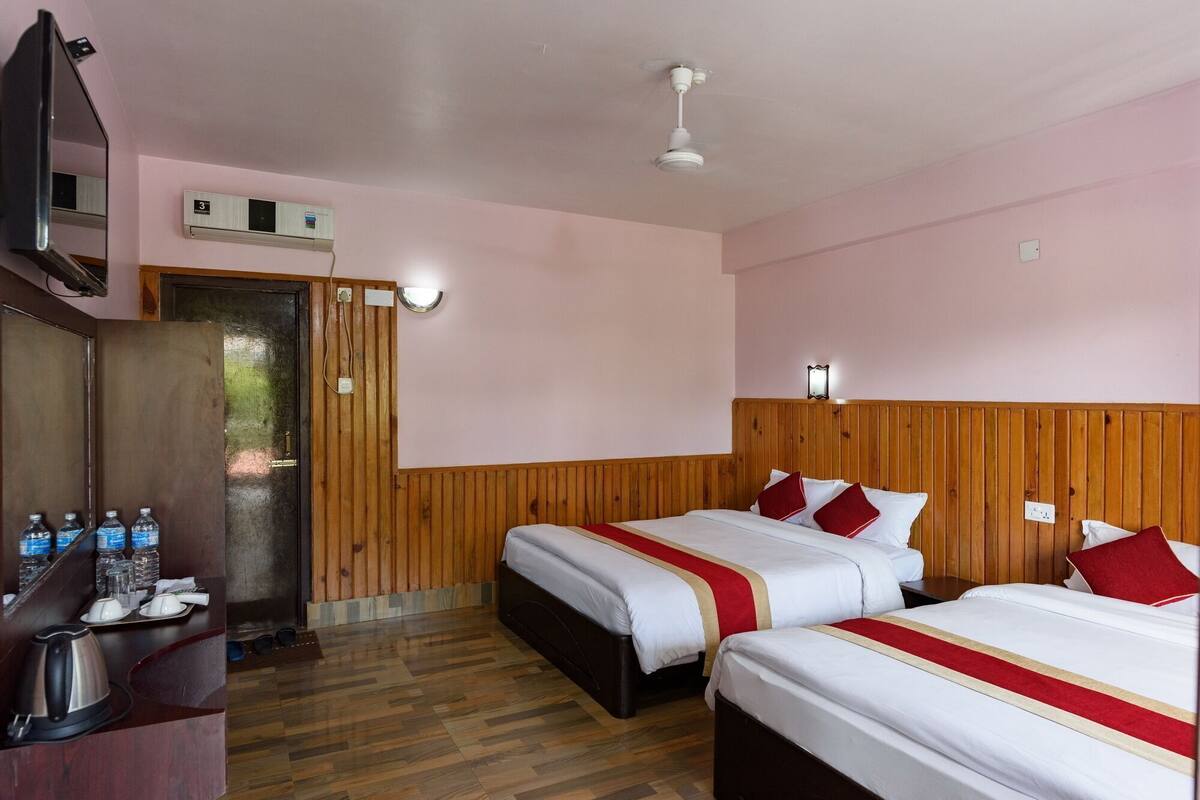 A hotel room with two beds, wooden paneling, a wooden desk with a kettle, and a mirror.