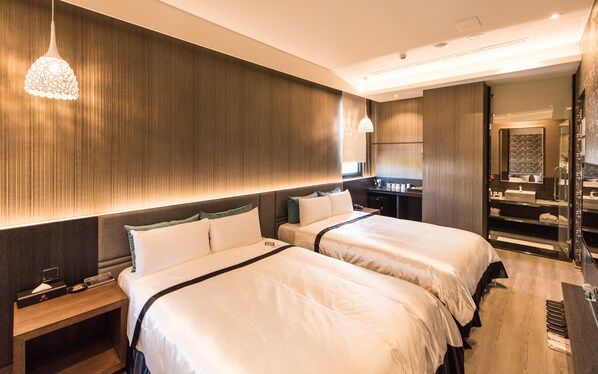 A hotel room with two beds, a nightstand, a desk with a lamp, and a bathroom visible through an open door. - Voga Motel (Taichung)