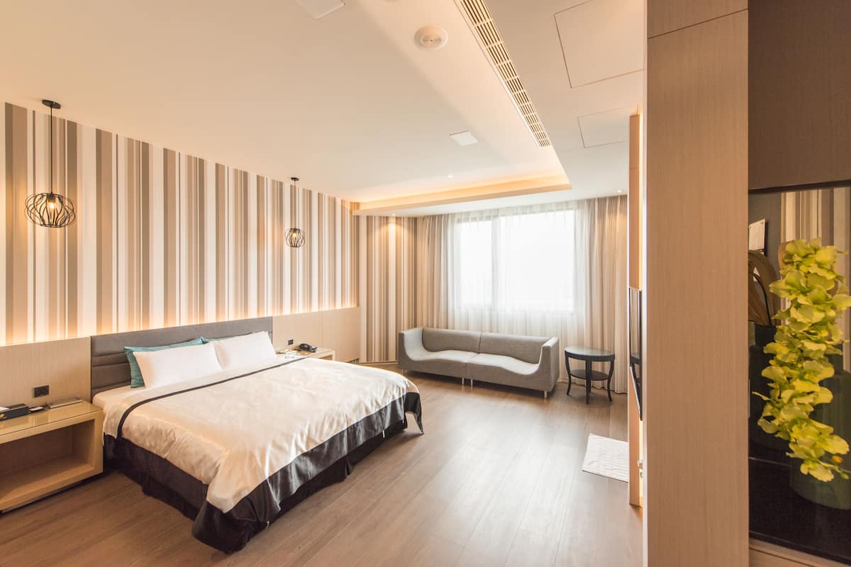 A modern hotel room with a large bed, a sofa, a small table, and a plant.