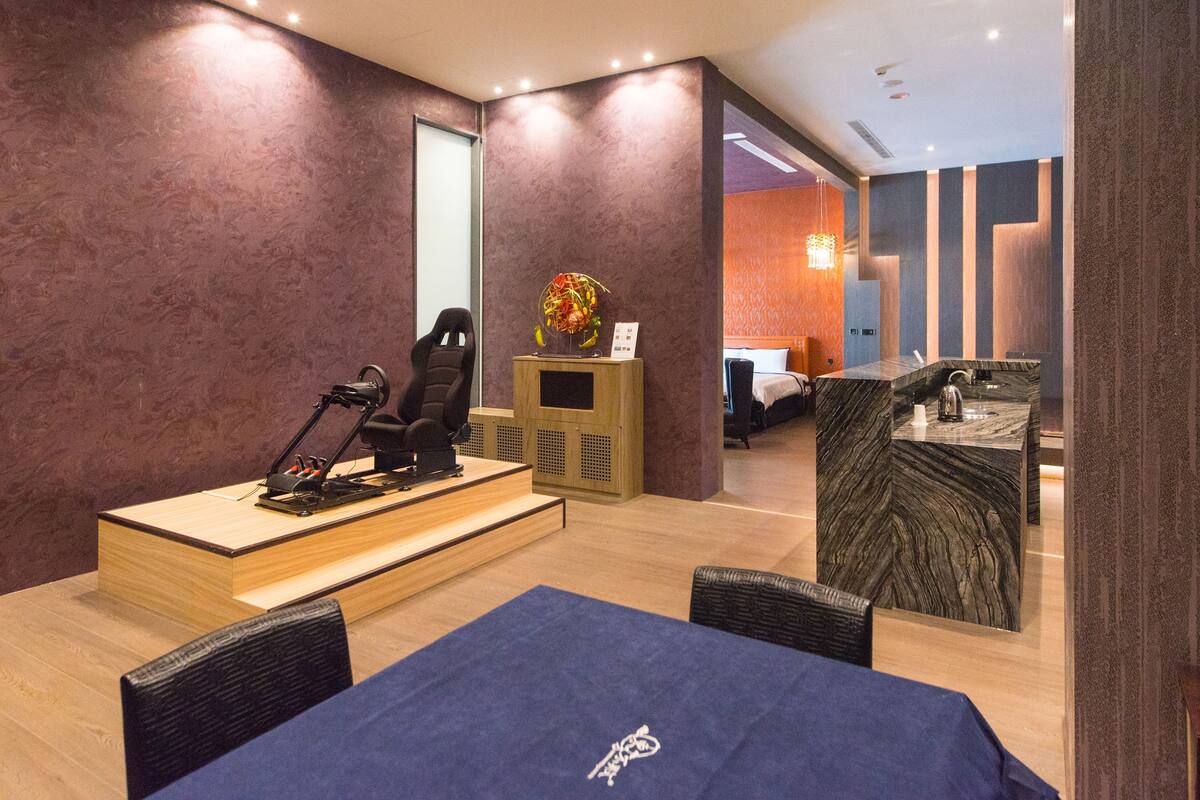 A hotel room with a gaming setup, a bed, a desk, and a bathroom visible through an open door.