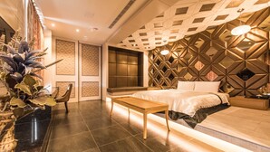 A modern hotel room with a large bed, a wooden nightstand, a seating area, and a decorative wall with geometric patterns. - Voga Motel (Taichung)
