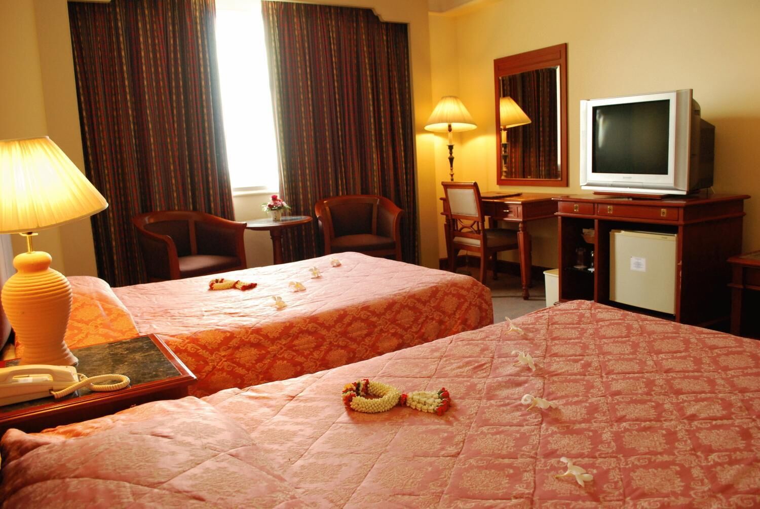 A hotel room with two beds, a desk, a chair, a television, and a lamp.