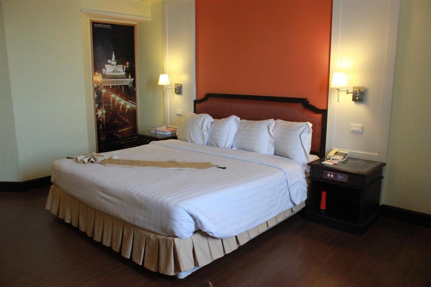 A hotel room with a large bed, two bedside tables, a nightstand, and a poster on the wall.
