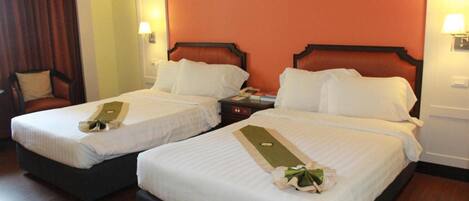 Habitación de hotel con dos camas, cada una con ropa blanca y una toalla verde. Hay mesitas de noche con lámparas y un aparador con teléfono.