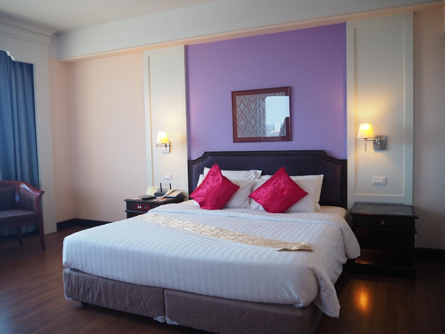 Habitación de hotel con una cama grande, dos mesitas de noche, un sillón y un espejo en la pared.