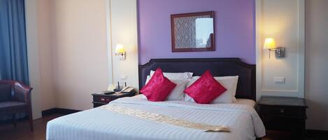 Habitación de hotel con una cama grande, dos mesitas de noche, un sillón y un espejo en la pared.