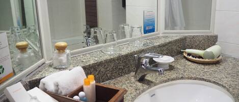 A bathroom with a granite countertop, a sink, a mirror, and a shower area.