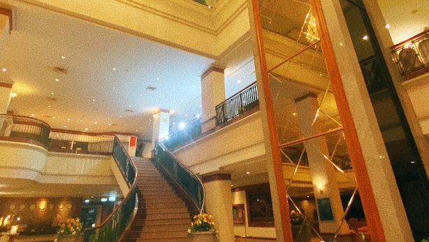 Ein mehrgeschossiges Interieur mit einer zentralen Treppe, Glasgeländern und Zierpflanzen.