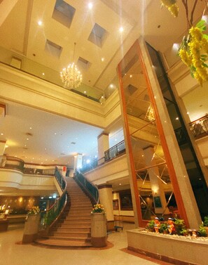 Un interior de varios niveles con una escalera central, barandas de vidrio y plantas decorativas.