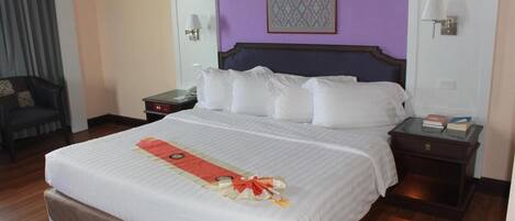 A hotel room with a large bed, a chair, a nightstand, and a wall-mounted lamp.