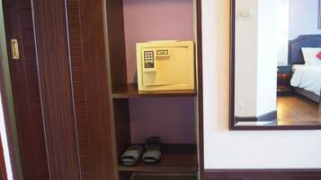 A hotel room with a wooden wardrobe, a small safe, and a pair of binoculars on the lower shelf.