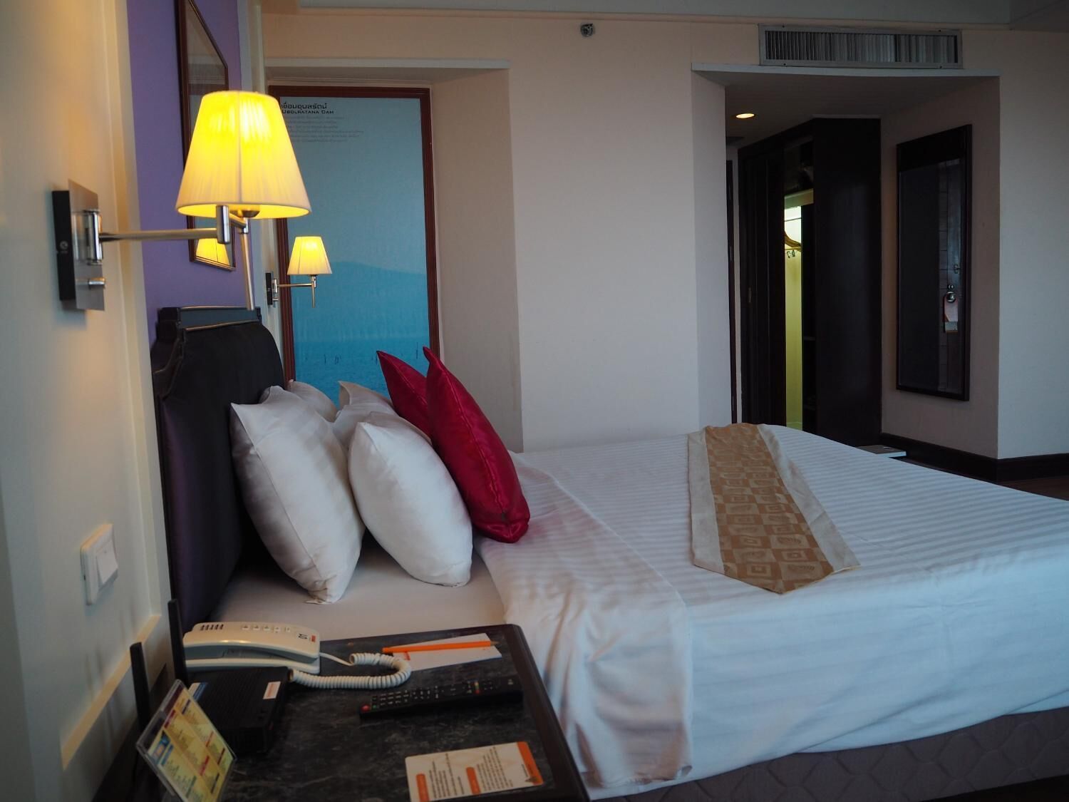 Habitación de hotel con cama, mesita de noche con lámpara, teléfono y control remoto.