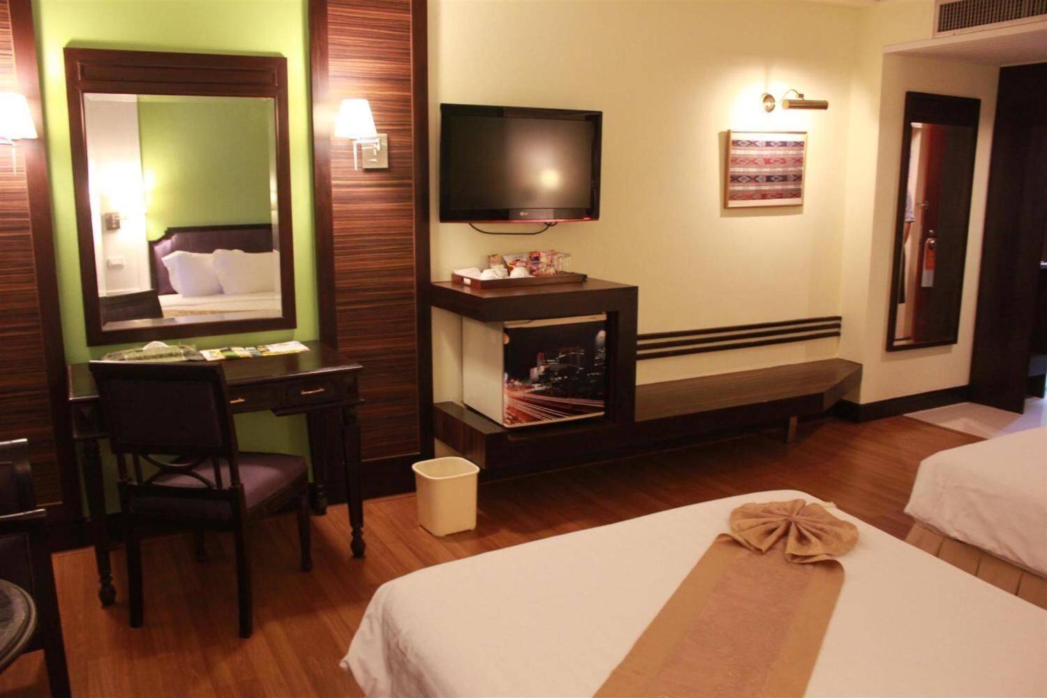 A hotel room with a bed, a desk with a chair, a television, a small table with a lamp, and a trash bin.