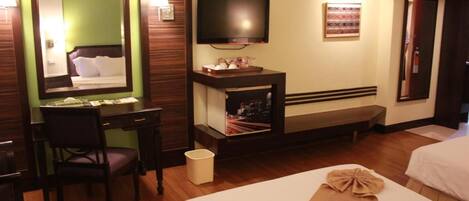 A hotel room with a bed, a desk with a chair, a television, a small table with a lamp, and a trash bin.