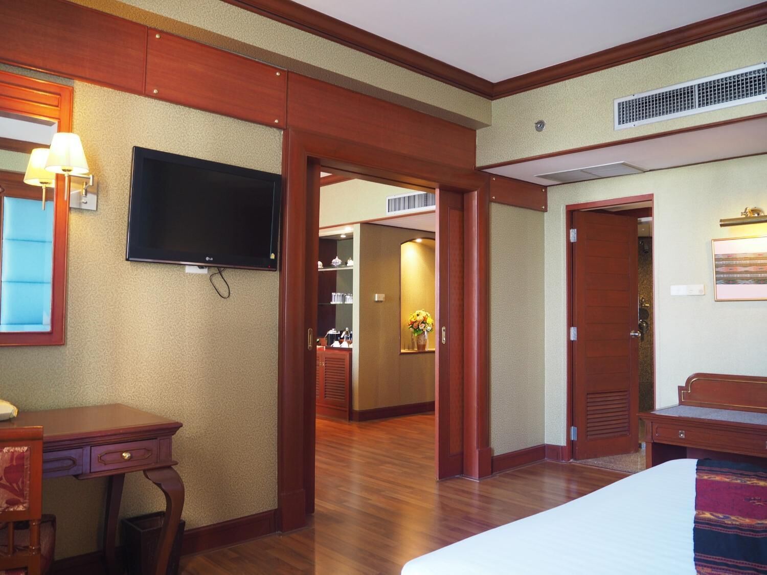 A hotel room with a bed, a desk, a TV, and a bathroom visible through an open door.