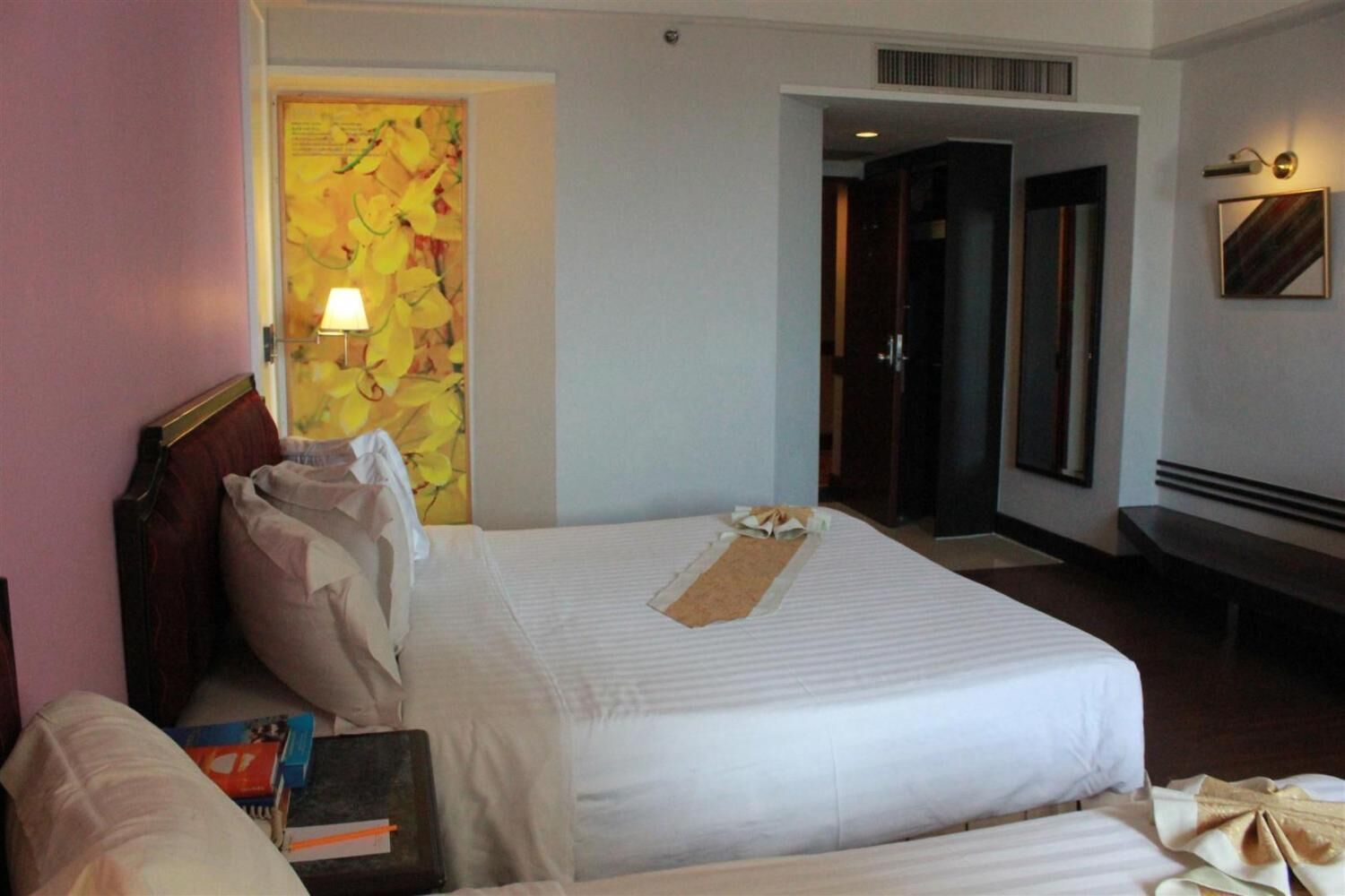 A hotel room with a large bed, a bedside table, a lamp, and a wall with a floral artwork.