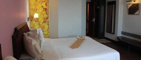 A hotel room with a large bed, a bedside table, a lamp, and a wall with a floral artwork.