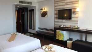 Ein Hotelzimmer mit zwei Betten, einem Schreibtisch mit Computer, einem Fernseher und einem kleinen Kühlschrank.