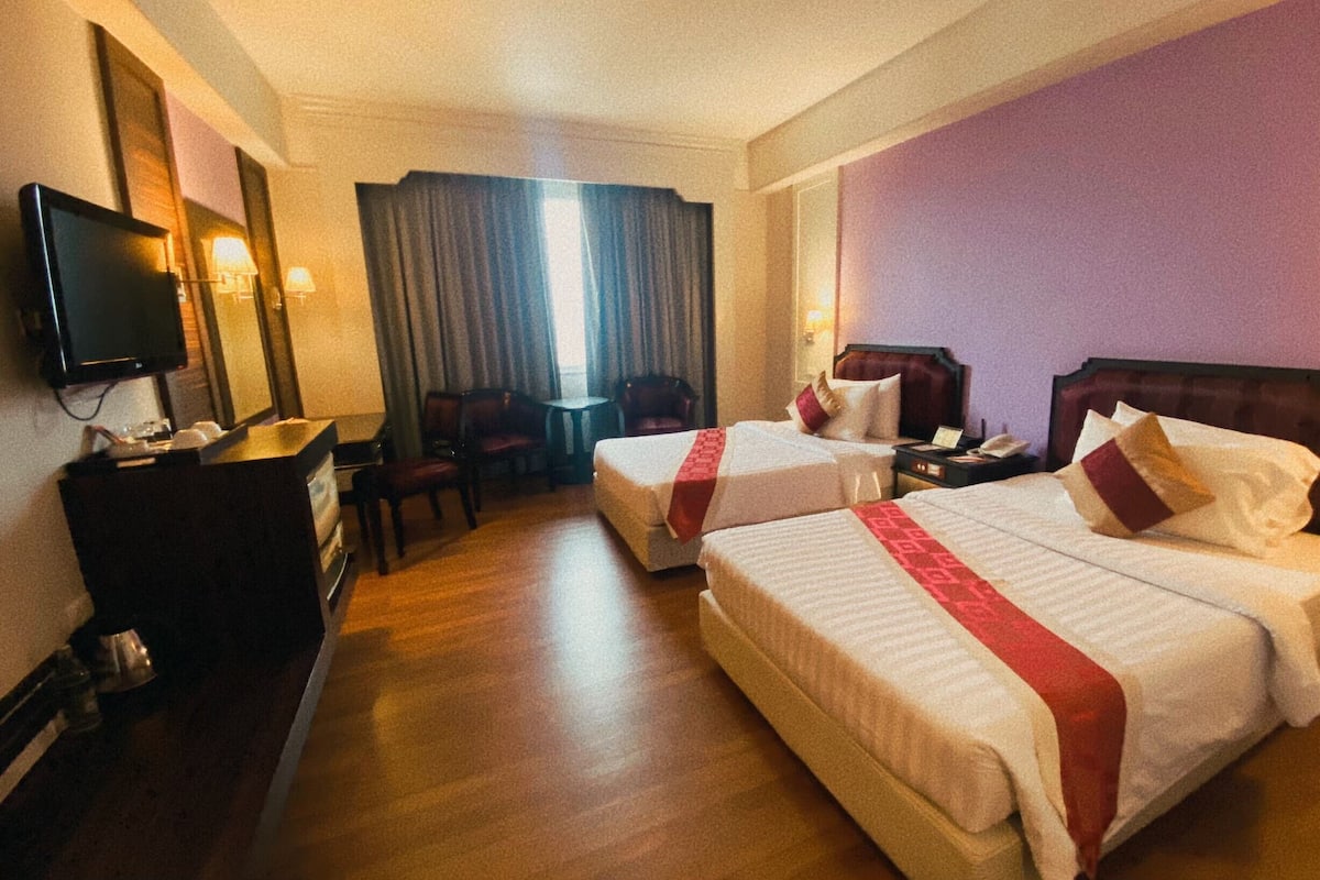 Quarto de hotel com duas camas, televisão, escrivaninha e uma cadeira.