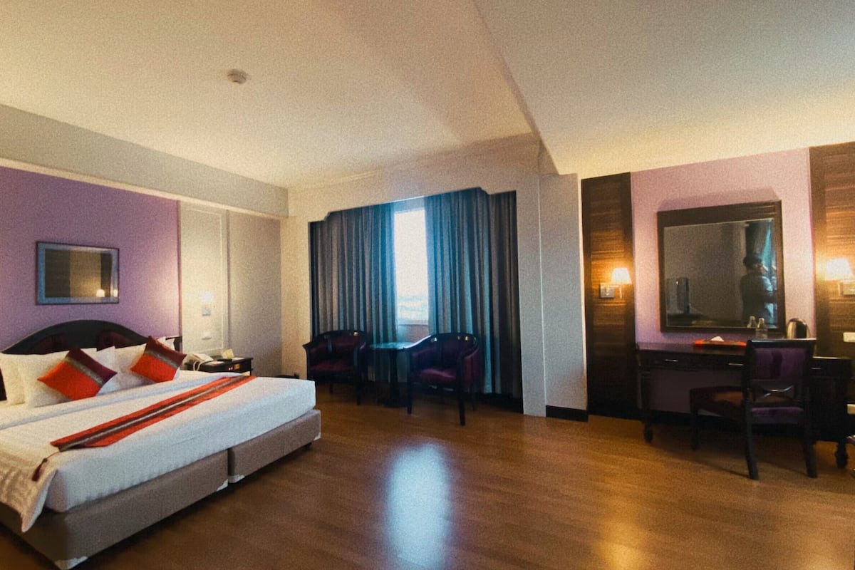 Quarto de hotel com uma cama grande, duas cadeiras, uma escrivaninha e um espelho.