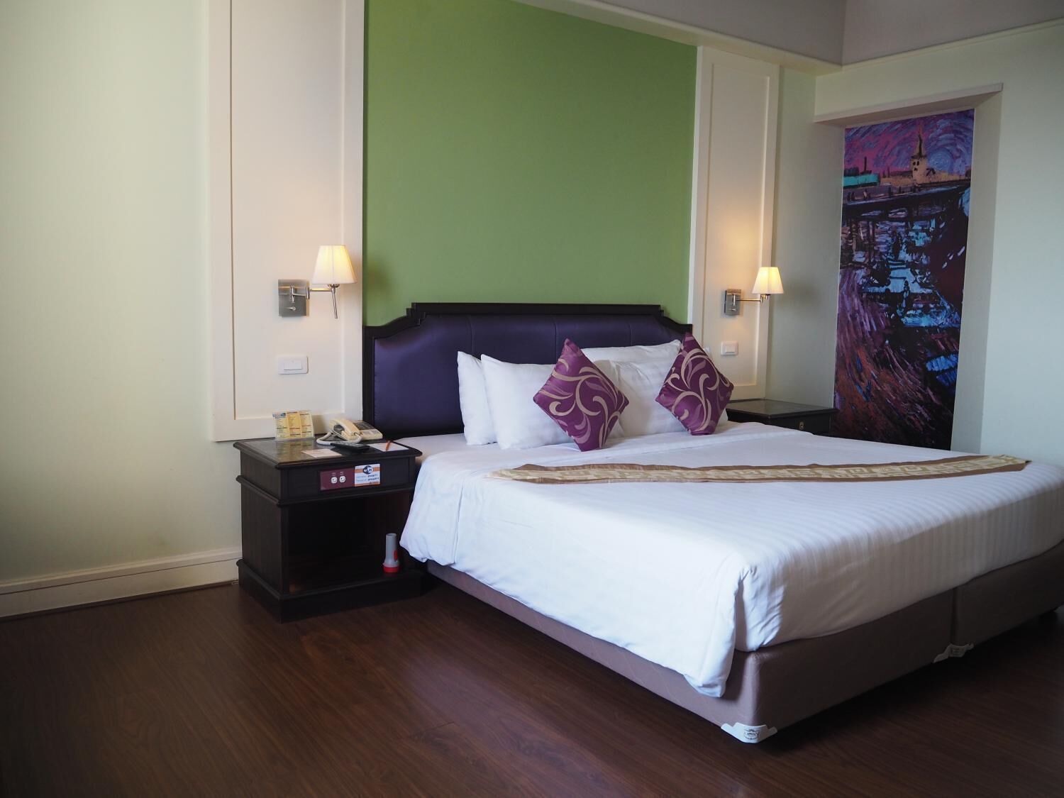 A hotel room with a large bed, two bedside tables, a green accent wall, and a painting on the wall.