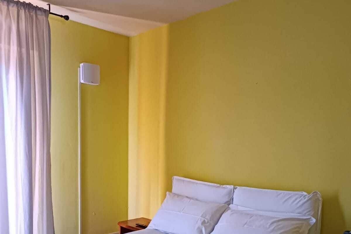 A bed with white and blue bedding, a bedside table, a lamp, and a wall-mounted light fixture in a room with yellow walls.