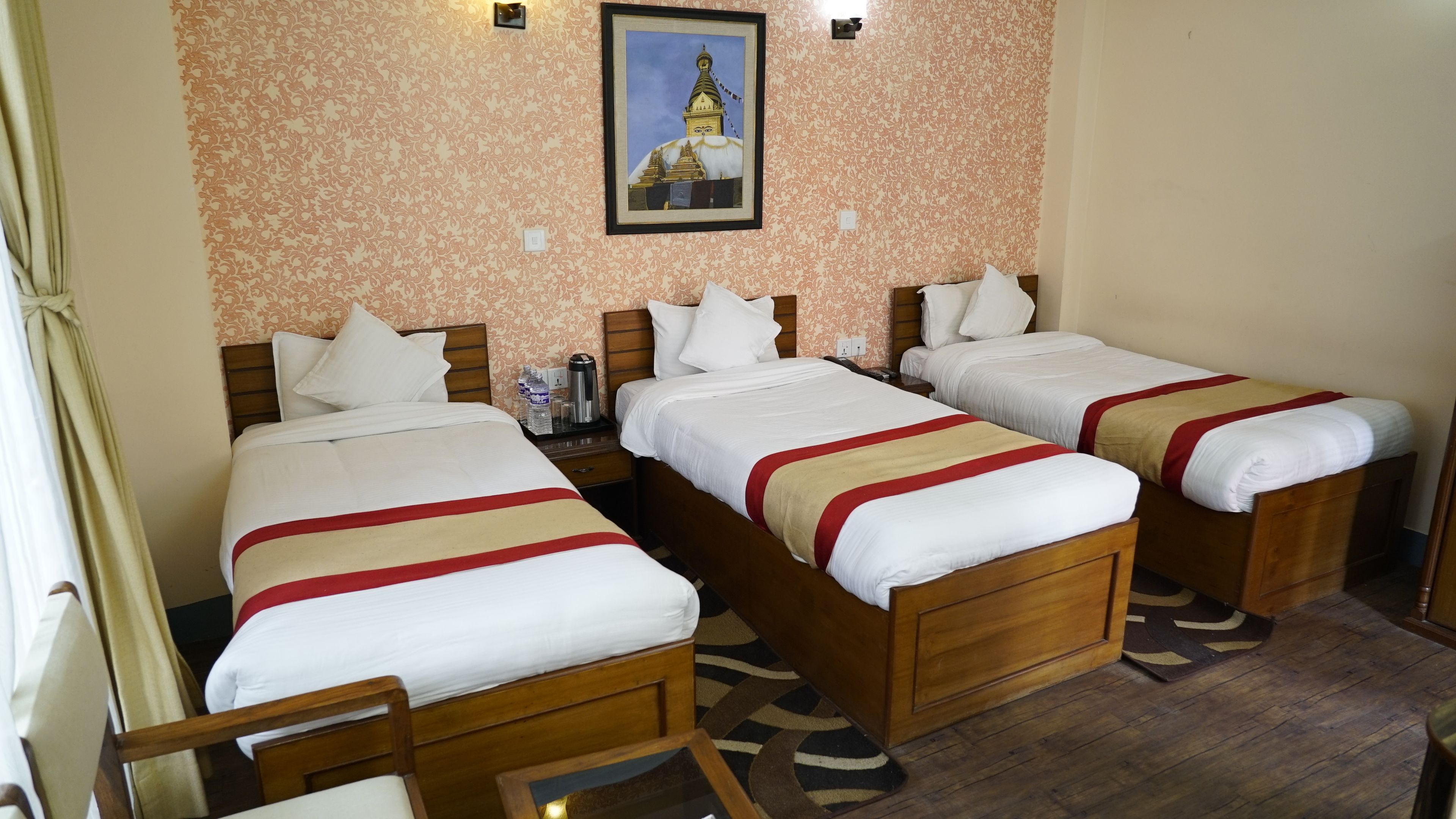 A hotel room with three single beds, wooden headboards, and a patterned wall.